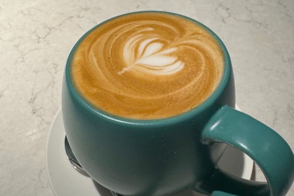 Freshly poured hot latte with latte art served in a teal ceramic mug on a counter-